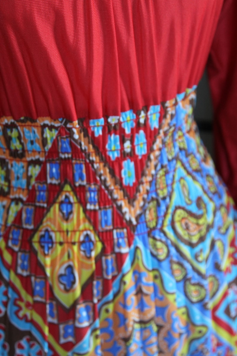 K&ouml;nnte beinhalten: Ein rotes Kleid mit einem bunten geometrischen Muster. Das Kleid hat ein tailliertes Oberteil und einen flie&szlig;enden Rock.