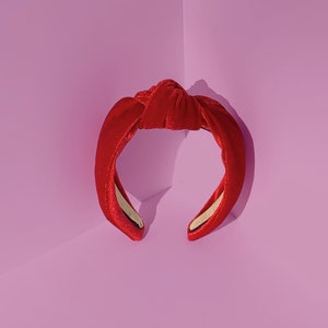Könnte beinhalten: Ein rotes Samt-Haarband mit einem Knotendesign. Das Haarband ist aus einem weichen, dehnbaren Material gefertigt und perfekt, um jedem Outfit einen Hauch von Eleganz zu verleihen.