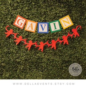 K&ouml;nnte beinhalten: Ein farbenfrohes Banner mit dem Namen "GAVIN" in Blockbuchstaben. Die Buchstaben sind an einer Schnur mit roten Affen-Ausschnitten befestigt.