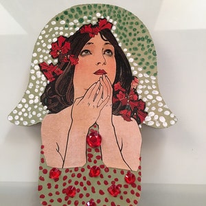 May include: A green and white hamsa hand with a red and white floral design and red rhinestones. The hamsa hand is a symbol of protection and good luck.