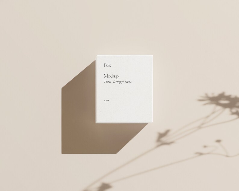 Pu&ograve; includere: Mockup di scatola quadrata bianca con il testo "Box Mockup Your image here PSD" su uno sfondo beige con l'ombra di una pianta.
