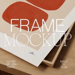 May include: A framed print with an abstract design featuring two red shapes on a beige background. The frame is made of wood and has a natural finish. The text "FRAME MOCKUP" is printed on the print. The text "CLOSE UP - DIN RATIO" is printed on the bottom left corner of the print. The text "MADE BY ROW" is printed on the bottom right corner of the print.