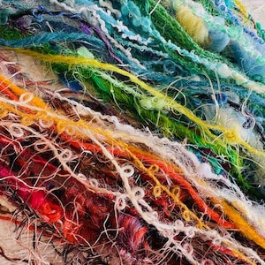 May include: Close-up of a vibrant mix of yarn in red, orange, yellow, green, blue, and white. The yarn displays diverse textures, including smooth, fuzzy, and looped. This yarn is likely intended for crafts like knitting or crochet.
