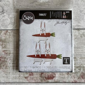 May include: Sizzix Thinlits die set with three white rabbits on carrots. The set includes 11 dies. The packaging features the text "Jim Holtz" and "11 DIES | 11 MATRICES | 11 TROQUELES | 11 FUSTELLE".