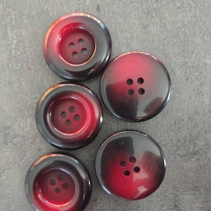 May include: Five large, round buttons with a two-tone design. The buttons have a dark brown outer ring that fades into a deep red center. Each button has four holes for sewing, and they are arranged in a symmetrical pattern.