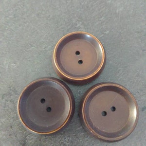 May include: Three large, dark brown buttons with a slightly raised center and two holes each. The buttons have a metallic gold-colored rim. These buttons are suitable for sewing projects.