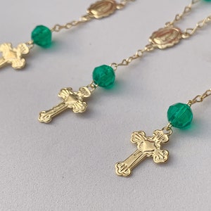 Puede incluir: Cadena de oro con cuentas de vidrio verde y cruces de oro. La cadena tiene peque&ntilde;os medallones con una imagen religiosa.