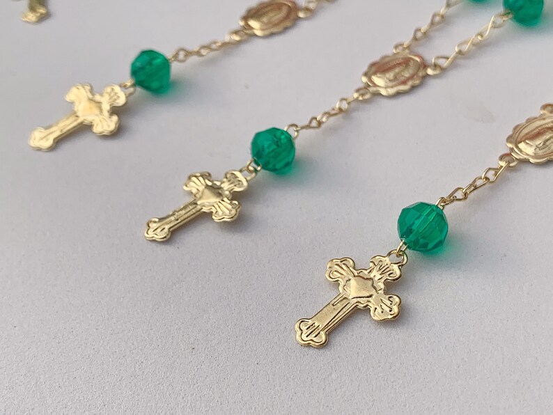 Puede incluir: Cadena de oro con cuentas de vidrio verde y cruces de oro. La cadena tiene peque&ntilde;os medallones con una imagen religiosa.