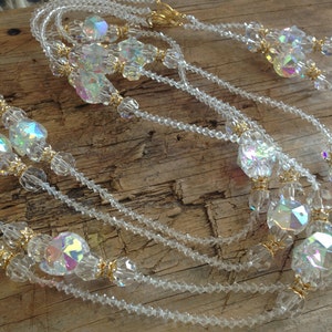 May include: A multi-strand necklace made of clear iridescent beads with gold accents. The necklace is made of multiple strands of small beads and larger, faceted beads.