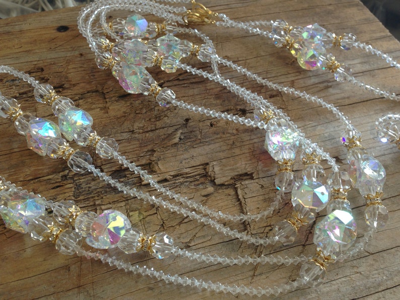 May include: A multi-strand necklace made of clear iridescent beads with gold accents. The necklace is made of multiple strands of small beads and larger, faceted beads.