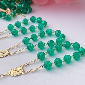 Puede incluir: Tres rosarios de cuentas de vidrio verde con detalles en metal dorado. Cada rosario tiene un peque&ntilde;o colgante dorado con una imagen religiosa.
