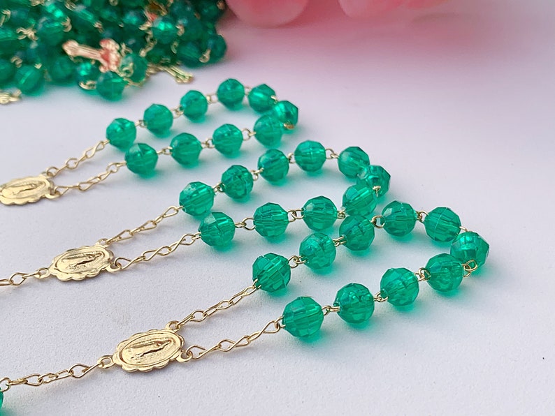 Puede incluir: Tres rosarios de cuentas de vidrio verde con detalles en metal dorado. Cada rosario tiene un peque&ntilde;o colgante dorado con una imagen religiosa.