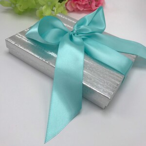 May include: A silver gift box with a light blue satin ribbon tied in a bow.