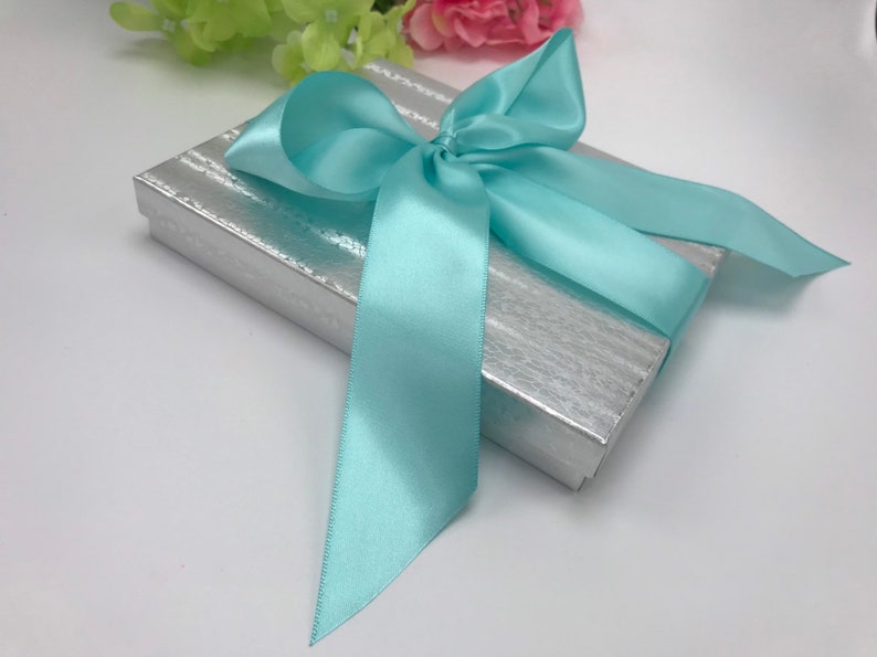 May include: A silver gift box with a light blue satin ribbon tied in a bow.