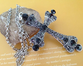 May include: A silver chain necklace with a large black and silver cross pendant. The cross is decorated with rhinestones and black beads.