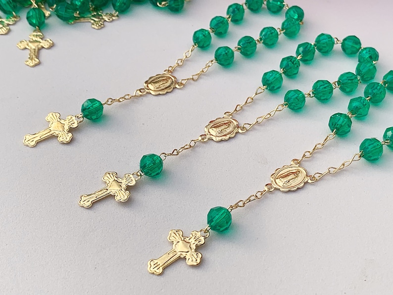 Puede incluir: Tres rosarios de cuentas de vidrio verde con cadenas y cruces doradas. Cada rosario tiene un dije dorado con una representaci&oacute;n de la Virgen Mar&iacute;a.