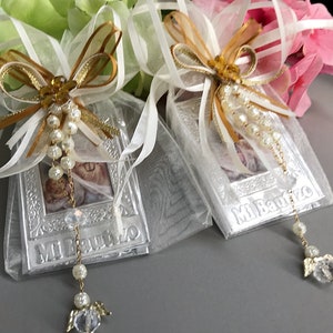 May include: Two white satin bags with gold ribbon bows and pearl chains. Each bag contains a silver picture frame with a photo and the text "Mi Bautizo".