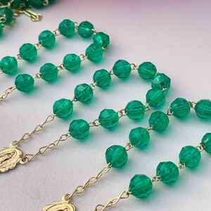 Puede incluir: Tres rosarios de cuentas de vidrio verde con cadenas y medallones de oro. Los rosarios est&aacute;n dispuestos sobre una superficie blanca.