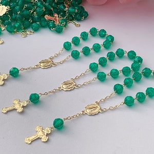 Puede incluir: Un conjunto de rosarios de cuentas de vidrio verde con detalles dorados. Cada rosario presenta una peque&ntilde;a cruz dorada y un dije ovalado dorado con una imagen religiosa.