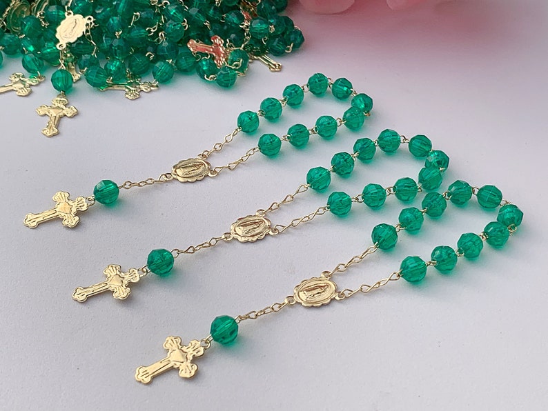 Puede incluir: Un conjunto de rosarios de cuentas de vidrio verde con detalles dorados. Cada rosario presenta una peque&ntilde;a cruz dorada y un dije ovalado dorado con una imagen religiosa.