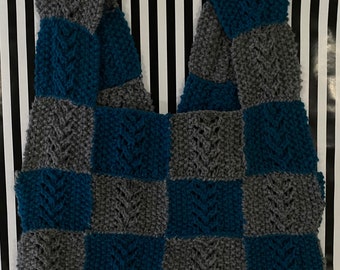 May include: A crocheted patchwork bag with a checkered pattern in teal blue and gray. The bag is made of yarn and has a unique, textured design.