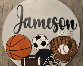 May include: A round, gray wooden sign featuring the name "Jameson" in black script, with "Dale" in white block letters. Sports-themed images include a basketball, soccer ball, baseball glove with ball, football, and helmet.