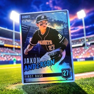 May include: A rectangular baseball trading card featuring a player in a black and gold Bandits uniform with the number 27. The card displays the name Jaxon Anderson, the position First Base, and a shield icon with the number 27 on a holographic surface.