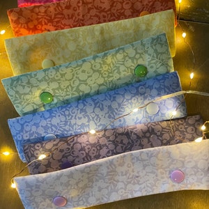 May include: A set of seven fabric face mask extenders in a rainbow of colours. Each extender has a floral pattern and a button on each end.