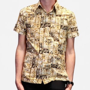 Puede incluir: Una camisa de manga corta con botones y un patrón geométrico marrón y blanco. El patrón presenta diseños repetidos de caras estilizadas y formas geométricas.