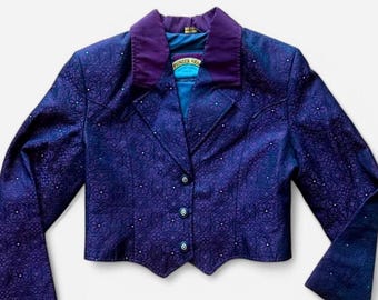 May include: A dark blue jacket with a floral pattern and a purple collar. The jacket has three buttons and small white embellishments. The label reads "Pioneer Wear".