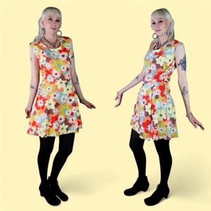 以下が含まれることがあります： カラフルな花柄のプリントが施されたノースリーブドレス。ドレスはフィットしたボディスとフレアスカートになっています。モデルは黒いタイツと黒い靴を履いています。