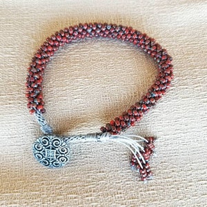 May include: A red beaded bracelet with a silver toggle clasp. The bracelet is made of small, round beads that are strung together in a tight pattern.