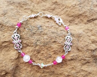 Puede incluir: Un brazalete de plata con cuentas rosas y transparentes, con dos abalorios de plata adornados con brillantes rosas. El brazalete tiene un cierre de mosquetón.