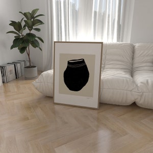 May include: A framed print of a black and white illustration of a round ceramic pot with a white rim. The pot is sitting on a beige background.