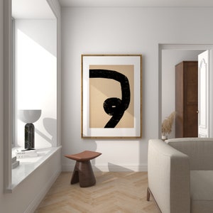 May include: A framed abstract art print with a black line drawing on a beige background. The print is hanging on a white wall above a wooden stool.