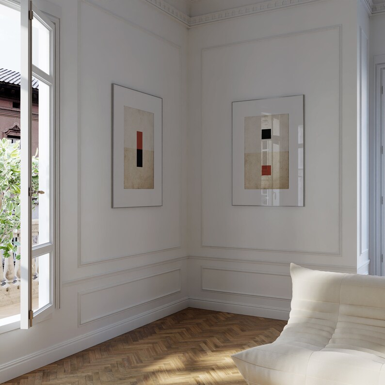 Op de afbeelding: Twee ingelijste abstracte schilderijen met geometrische vormen in rood, zwart en wit, hangend aan een witte muur in een kamer met een witte bank en een raam.