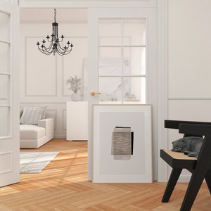 May include: A white room with a black chair and a black and white abstract print hanging on the wall. A cat is sleeping on the chair. The room has white walls and a wooden floor.