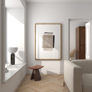 May include: A white room with a large window, a wooden stool, a beige sofa, and a framed abstract art print with brown and black geometric shapes.