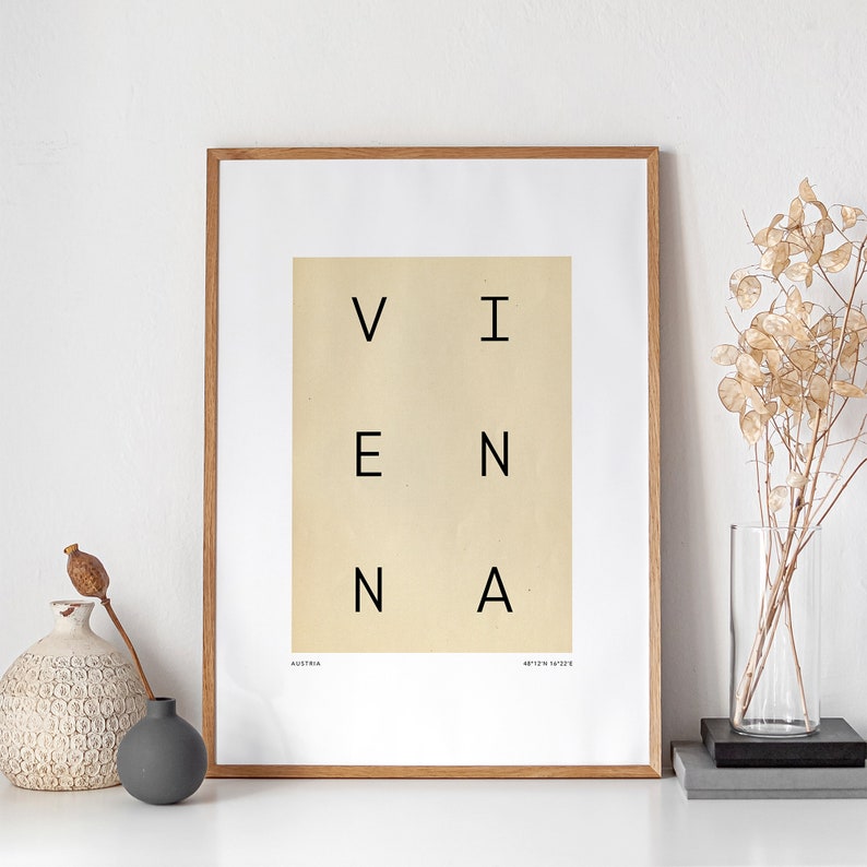 May include: A framed print with the word "VIENNA" spelled out in a grid pattern. The print is on a cream background with black text. The frame is a light brown wood.