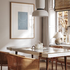 Op de afbeelding: Een eetkamer met een witte tafel met een witte en gouden inleg, vier gevlochten stoelen, een witte hanglamp en een ingelijst abstract print aan de muur.