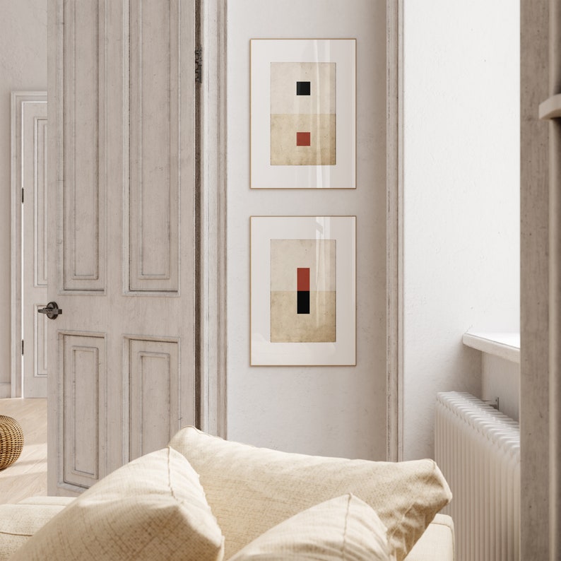 Op de afbeelding: Twee ingelijste abstracte kunstprints met geometrische vormen in zwart, rood en wit op een witte muur.