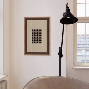 May include: A framed print with a black and white geometric pattern of triangles. The print is hanging on a white wall next to a black floor lamp with a black lampshade.