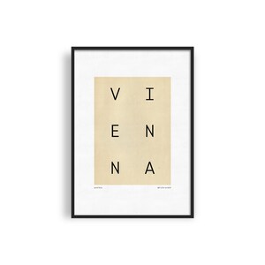 May include: A black framed print with a beige background and the word "VIENNA" spelled out in black letters. The words "AUSTRIA" and "ART PRINT 12x16" are printed in smaller font at the bottom of the print.