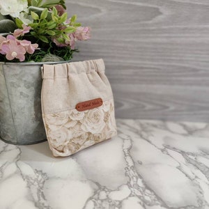 May include: A small, beige drawstring bag with a floral print of white roses. The bag has a brown leather tag that says "Hand Made".