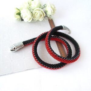 May include: A beaded snake necklace with a silver snake head charm. The necklace is made with black and red beads.