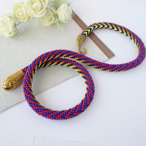 May include: A beaded snake necklace with a gold snake head clasp. The necklace is made with red, blue, yellow, and black beads.