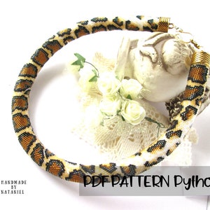 Könnte beinhalten: Eine röhrenförmige Perlenkette mit einem sich wiederholenden Pythonhautmuster in Braun-, Schwarz- und Cremetönen. Die Kette ist mit goldfarbenen Metallendkappen und einem Verschluss versehen. Der Text PDF PATTERN Python ist in der Ecke sichtbar.