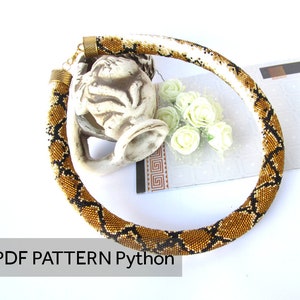 Könnte beinhalten: Eine röhrenförmige Perlenkette mit einem sich wiederholenden Pythonhautmuster in Gold, Braun und Schwarz. Die Kette hat metallische Endkappen und einen Verschluss. Der Text PDF PATTERN Python ist in der unteren linken Ecke zu sehen.