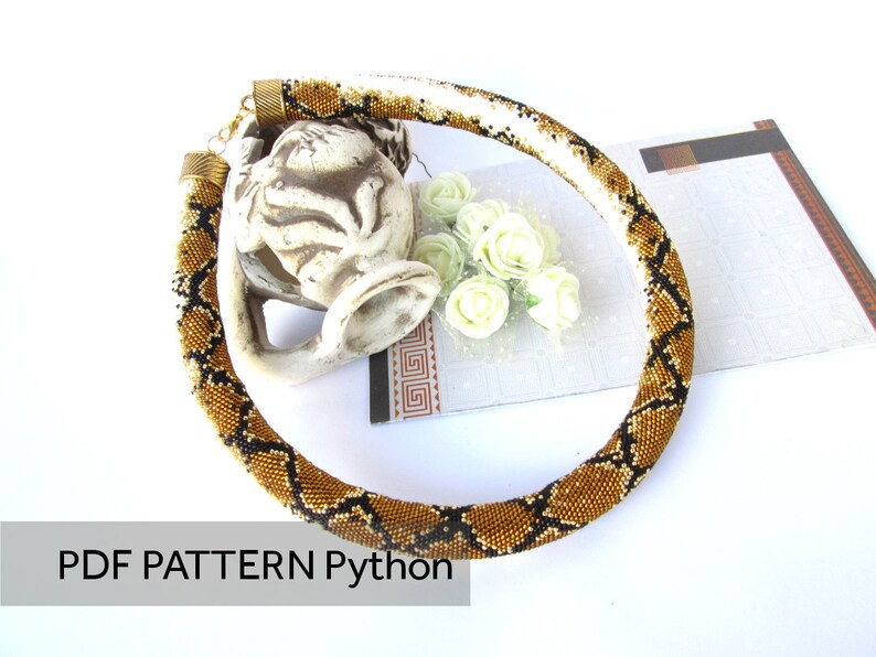 May include: A tubular beaded necklace featuring a repeating gold, brown, and black python skin pattern. The necklace has metallic end caps and a clasp. The text PDF PATTERN Python is visible in the lower left corner of the image.