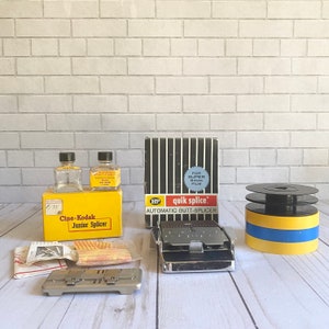May include: A yellow and black box labeled "Cine-Kodak Junior Splicer" with two clear glass bottles with yellow caps. The box is next to a black and white box labeled "HP quik splice. AUTOMATIC BUTT-SPLICER" for super 8mm film. There is a silver metal splicer and a yellow and blue film reel.